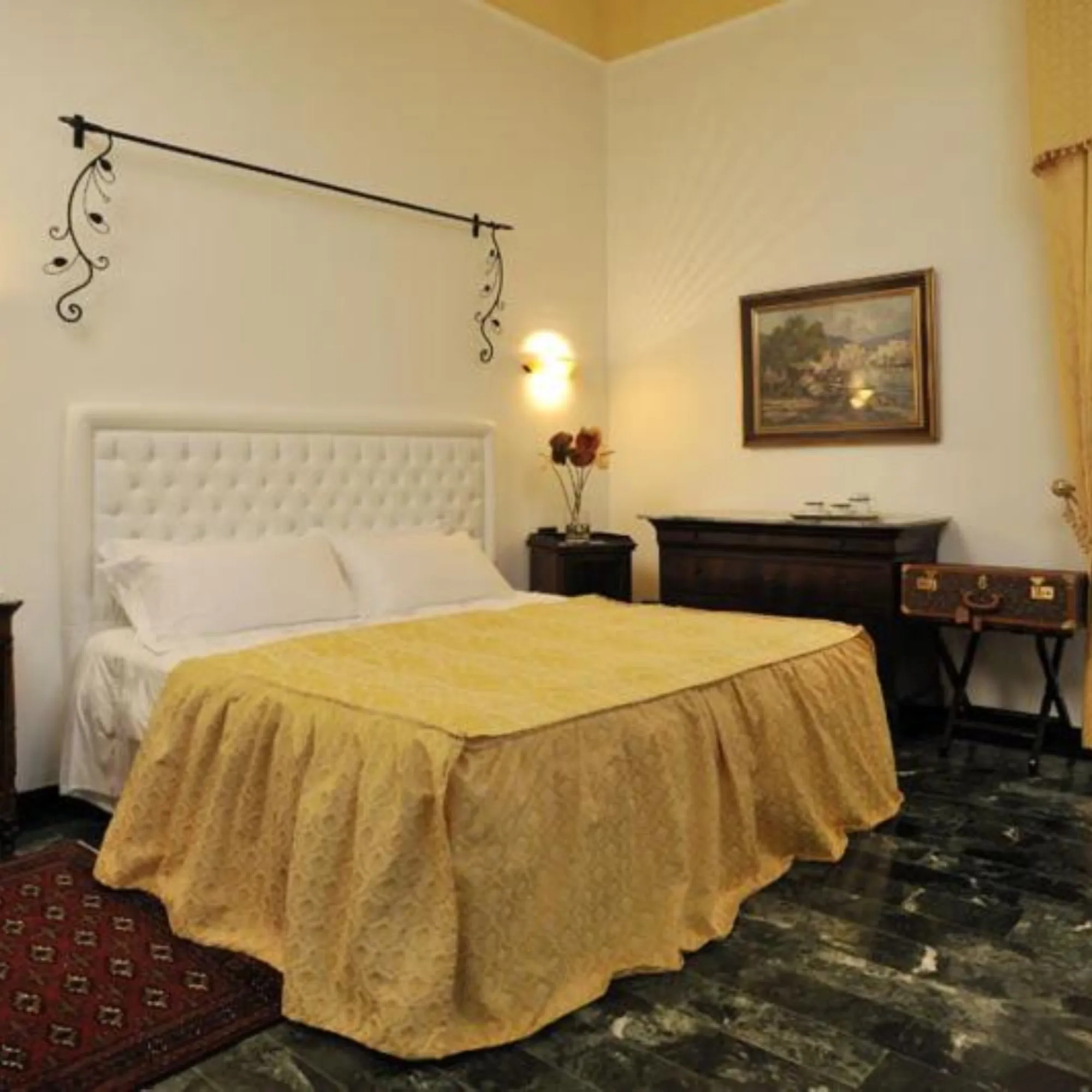 Letto matrimoniale di Villa Las Tronas Hotel & Spa con testiera bianca, tessuti dorati e arredi d'epoca su pavimento in marmo scuro.