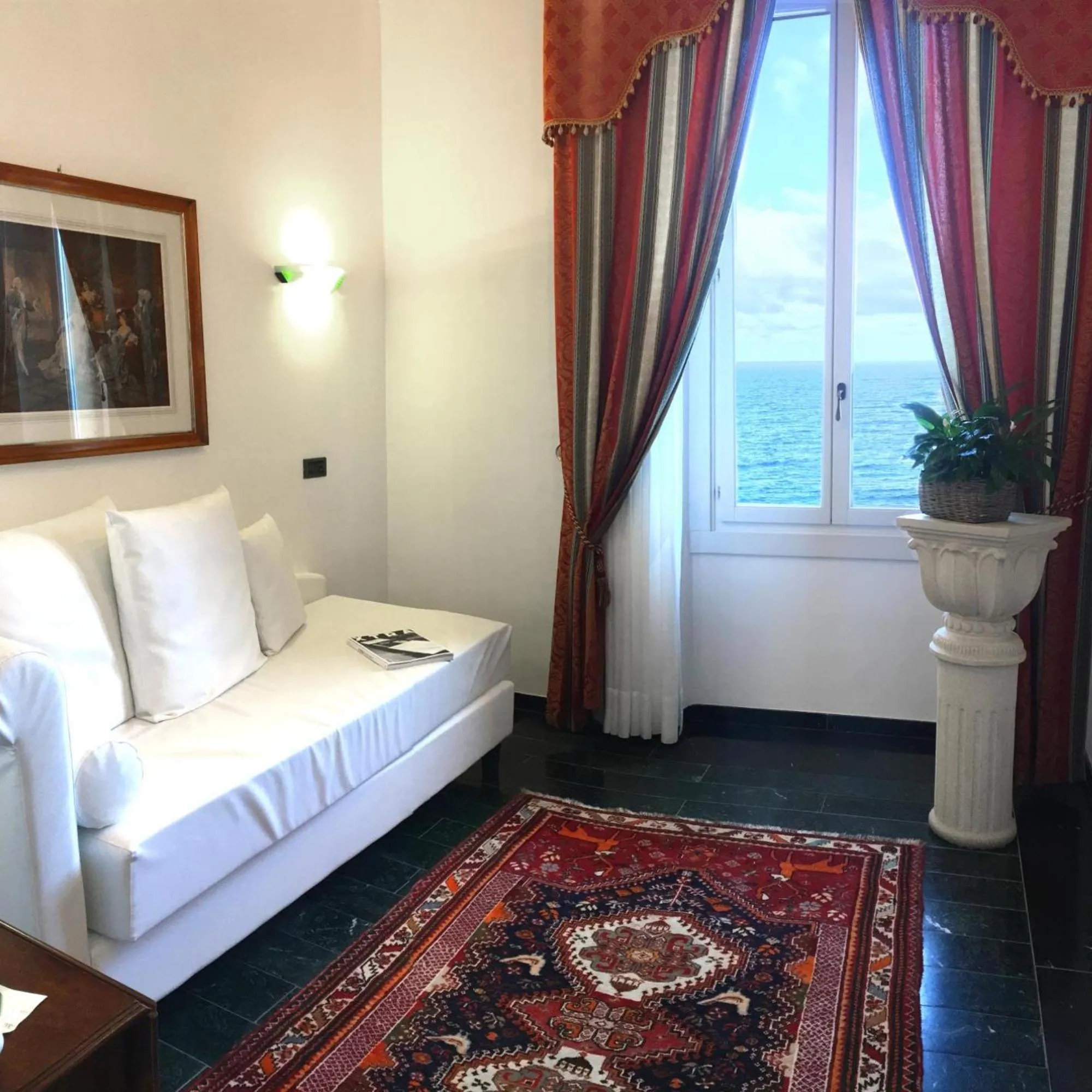 Salotto della Suite a Villa Las Tronas Hotel & Spa, con divano bianco, tappeto pregiato, colonna decorativa e finestra vista mare.