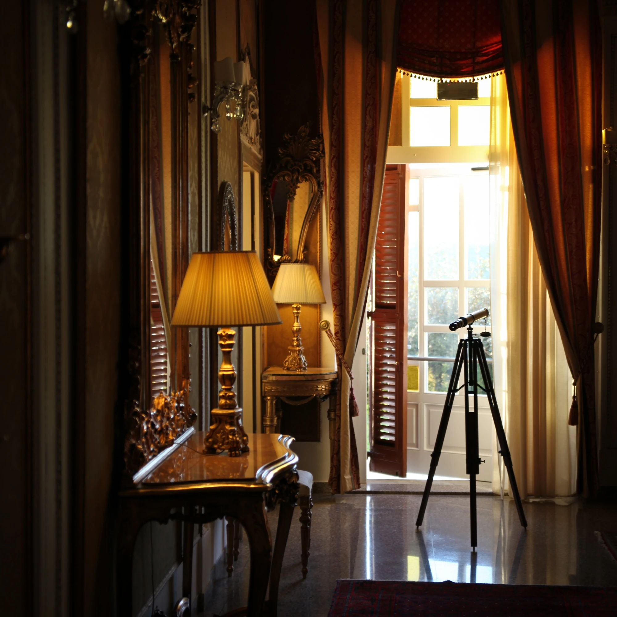 Salone nobile di Villa Las Tronas Hotel & Spa con telescopio antico, consolle dorata, lampade classiche e vista panoramica.