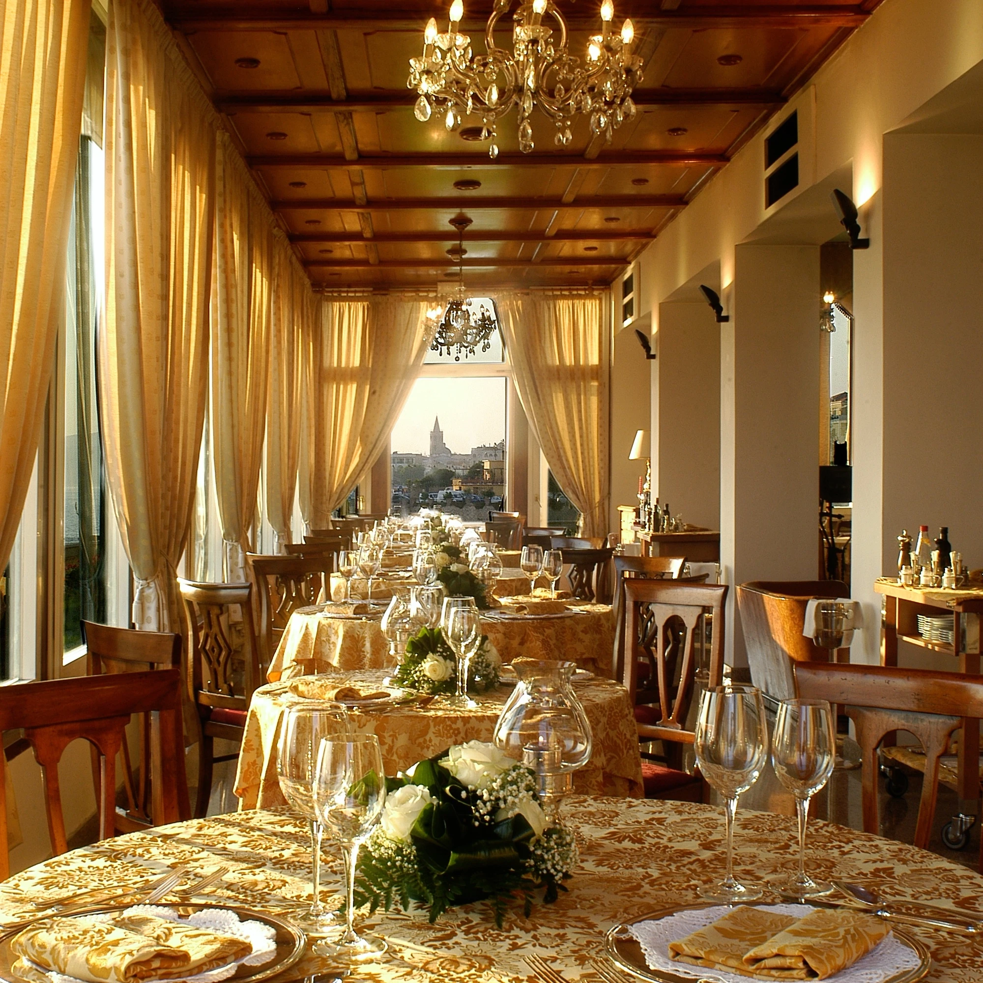 Elegante sala da pranzo per eventi a Villa Las Tronas Hotel & Spa, con lampadari di cristallo, tavole apparecchiate e vista panoramica su Alghero.