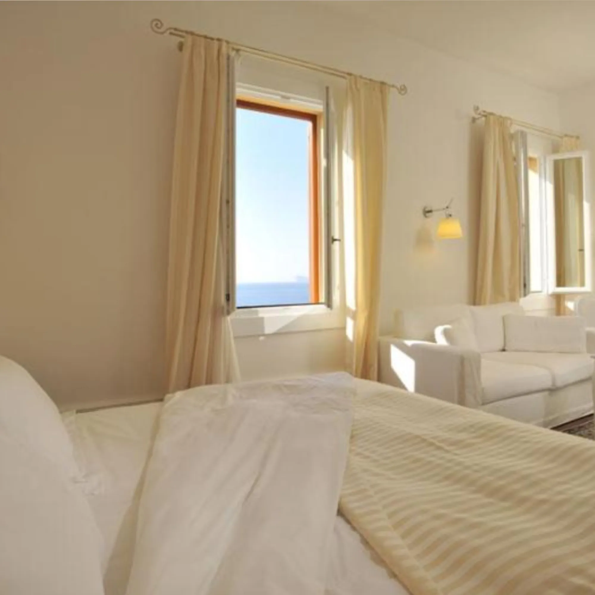 Particolare del letto matrimoniale nella Suite di Villa Las Tronas Hotel & Spa, con lenzuola bianche e finestra aperta sull'azzurro del mare.